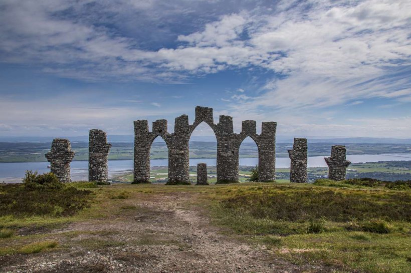 Fyrish Monument - Stone arches on top of a mountain with a view of the sea beyond.